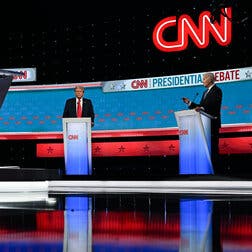 Donald Trump, left, and President Biden standing at lecterns on the debate stage. Their images are reflected in the shiny floor. 