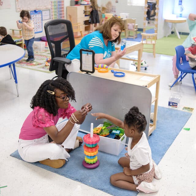 Michaela Frederick, a preschool teacher, plays with a stacking toy with a student.